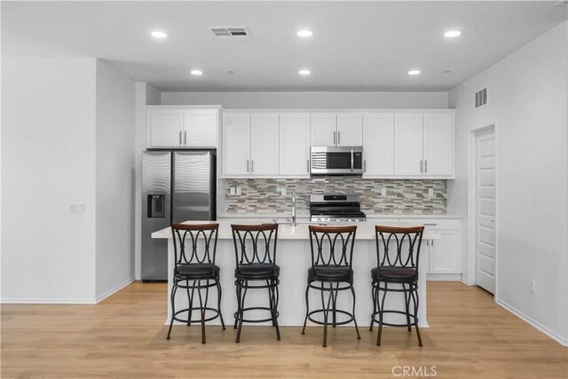 kitchen with a center island with sink, backsplash, white cabinets, and stainless steel appliances