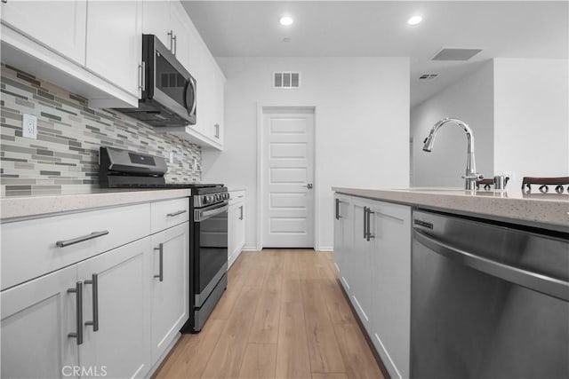 kitchen with light wood-type flooring, appliances with stainless steel finishes, decorative backsplash, and white cabinetry