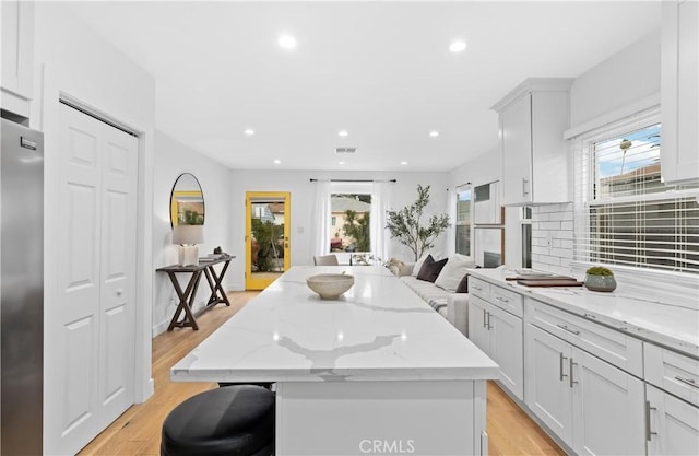 kitchen with light wood-type flooring, a kitchen island, stainless steel fridge, and light stone countertops