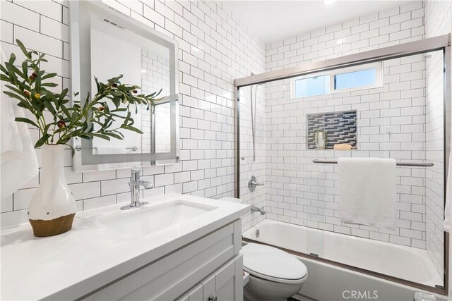 full bathroom featuring bath / shower combo with glass door, toilet, vanity, and tasteful backsplash