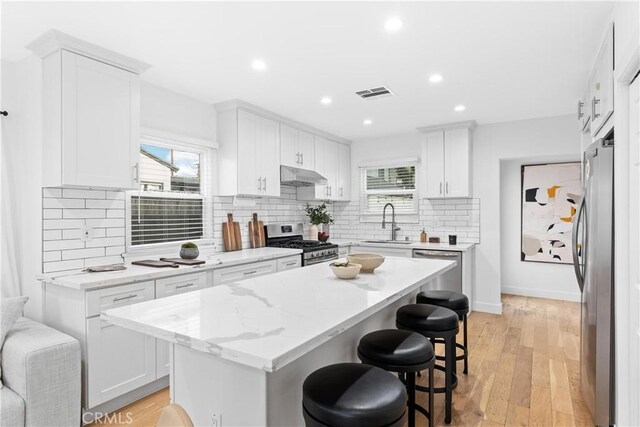 kitchen featuring appliances with stainless steel finishes, a kitchen island, white cabinetry, light stone counters, and a breakfast bar