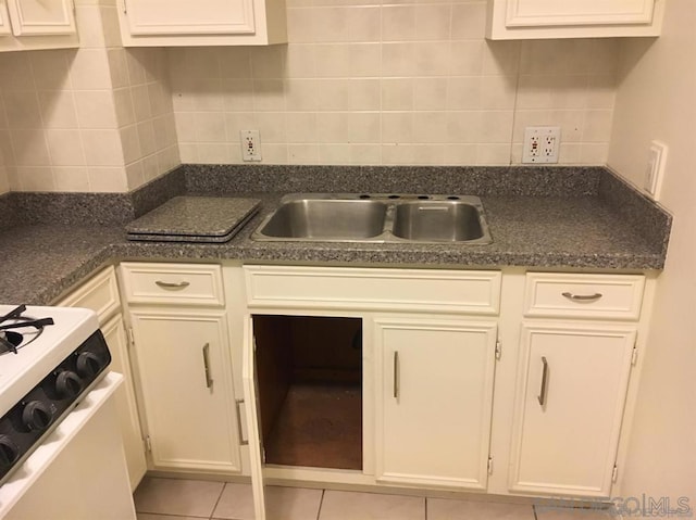 kitchen with sink, tasteful backsplash, white gas stove, light tile patterned flooring, and white cabinetry