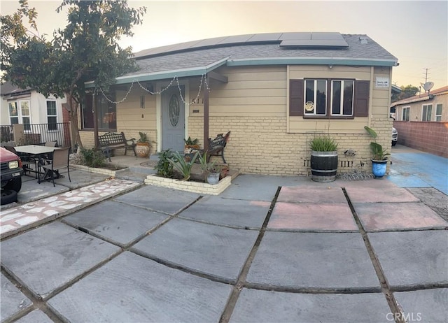 rear view of house featuring solar panels, brick siding, fence, roof with shingles, and a patio area