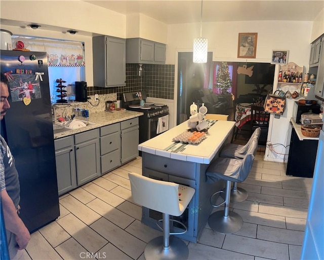 kitchen featuring backsplash, tile countertops, pendant lighting, a breakfast bar, and appliances with stainless steel finishes