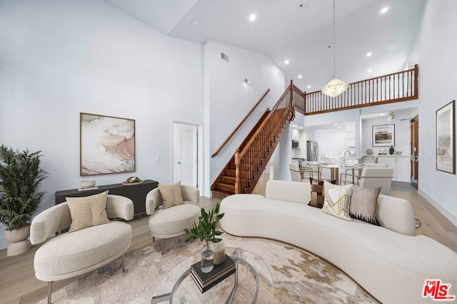 living room with high vaulted ceiling, an inviting chandelier, and light hardwood / wood-style flooring