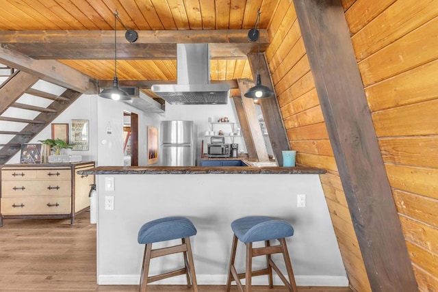 kitchen with a kitchen bar, hanging light fixtures, appliances with stainless steel finishes, kitchen peninsula, and island exhaust hood