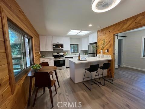 kitchen with white cabinetry, light hardwood / wood-style flooring, kitchen peninsula, wooden walls, and appliances with stainless steel finishes