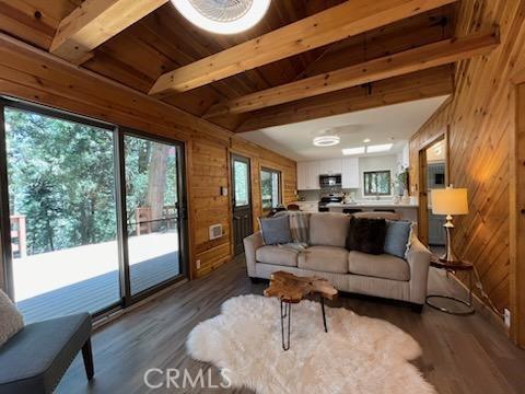 living room featuring beamed ceiling, wooden walls, wooden ceiling, and dark wood-type flooring