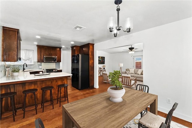 dining area with ceiling fan with notable chandelier, dark wood-type flooring, and sink