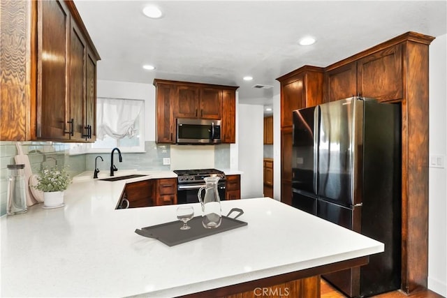 kitchen featuring sink, kitchen peninsula, a kitchen bar, decorative backsplash, and appliances with stainless steel finishes