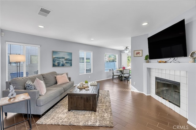 living room featuring a tile fireplace, dark hardwood / wood-style flooring, and ceiling fan