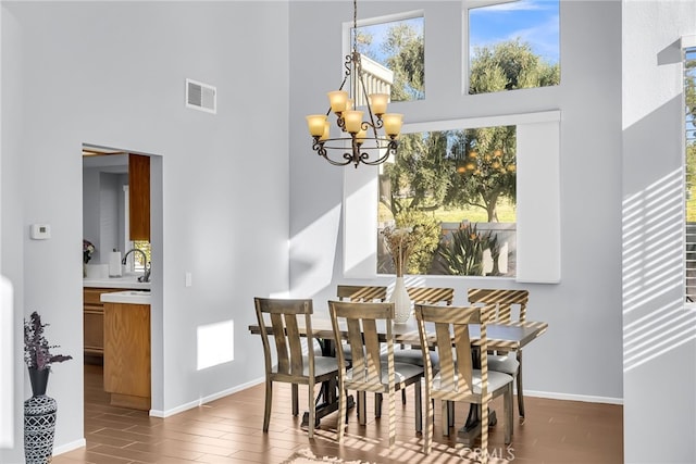 dining space with plenty of natural light, wood-type flooring, a high ceiling, and an inviting chandelier