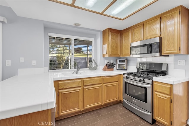 kitchen with stainless steel appliances, tile counters, dark wood-type flooring, and sink