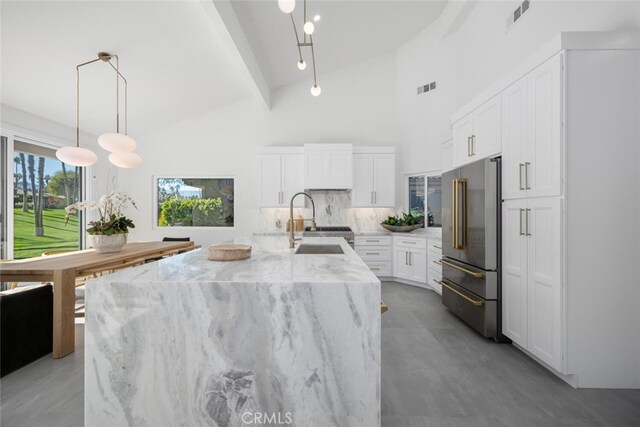 kitchen featuring sink, white cabinetry, high end refrigerator, pendant lighting, and a kitchen island with sink