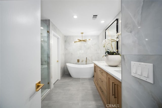 bathroom with an inviting chandelier, vanity, independent shower and bath, and tile walls