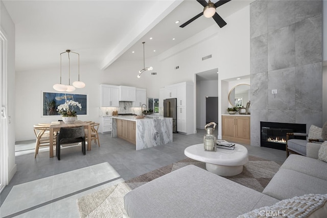 living room with a fireplace, sink, a high ceiling, ceiling fan, and beam ceiling