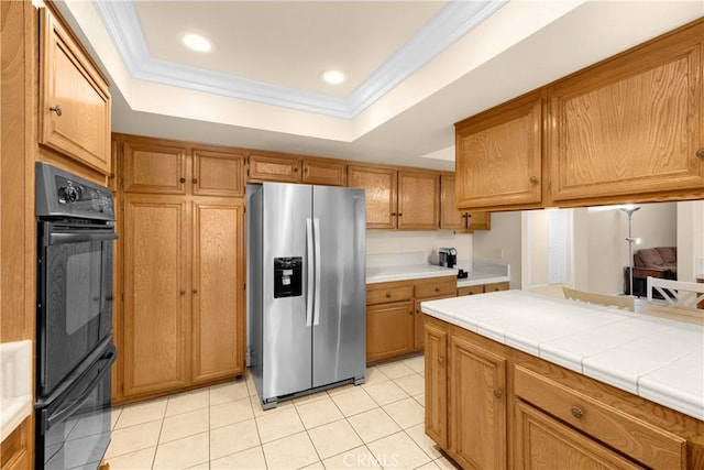 kitchen featuring tile countertops, stainless steel refrigerator with ice dispenser, black double oven, and a tray ceiling