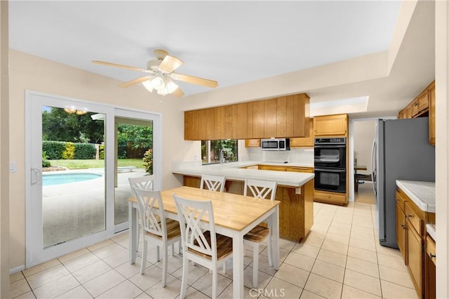 kitchen featuring kitchen peninsula, ceiling fan, light tile patterned floors, and appliances with stainless steel finishes