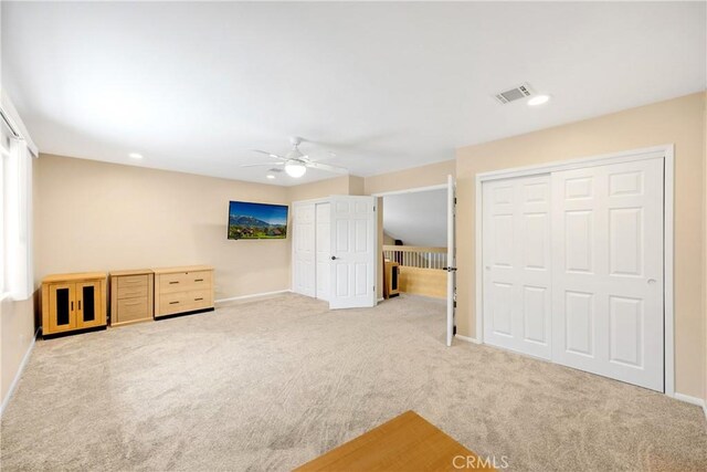 unfurnished bedroom with ceiling fan, light colored carpet, and two closets