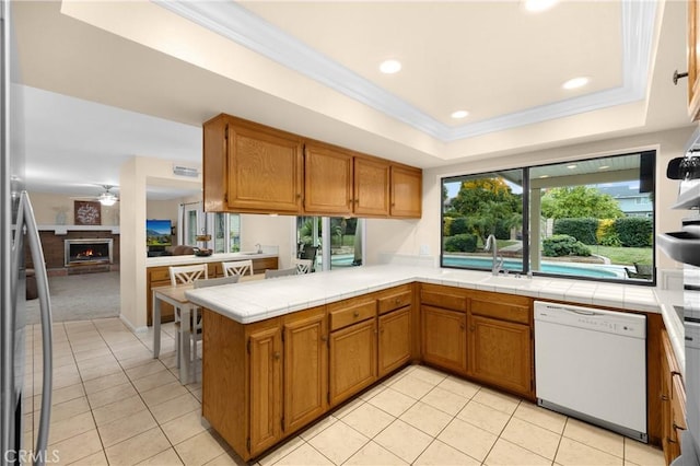 kitchen with kitchen peninsula, white dishwasher, a raised ceiling, ceiling fan, and sink