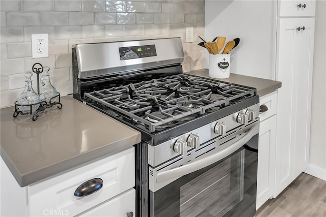 kitchen with tasteful backsplash, white cabinetry, dark wood-type flooring, and gas range