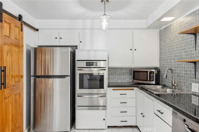 kitchen featuring a barn door, stainless steel appliances, a sink, white cabinets, and a warming drawer