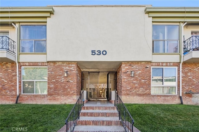 doorway to property with brick siding, a yard, and stucco siding