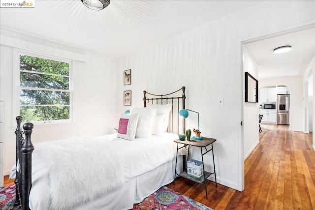 bedroom with dark hardwood / wood-style flooring and stainless steel refrigerator with ice dispenser