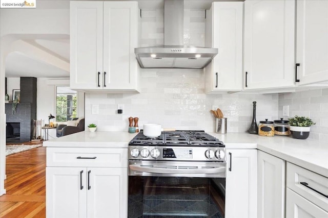 kitchen with tasteful backsplash, white cabinetry, wall chimney range hood, and stainless steel gas range