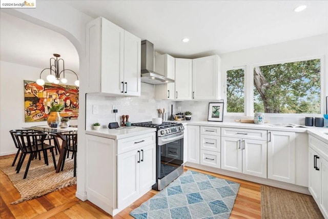 kitchen featuring tasteful backsplash, white cabinetry, wall chimney exhaust hood, gas stove, and light hardwood / wood-style flooring