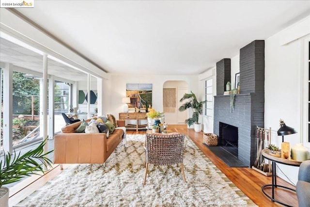 living room featuring wood-type flooring, a brick fireplace, and a healthy amount of sunlight