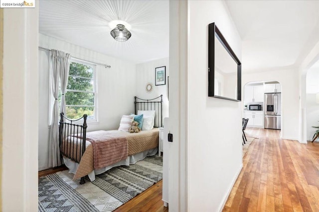 bedroom featuring stainless steel fridge and light hardwood / wood-style floors