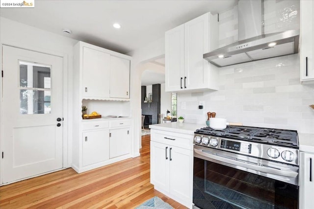 kitchen featuring white cabinets, wall chimney range hood, and stainless steel gas stove