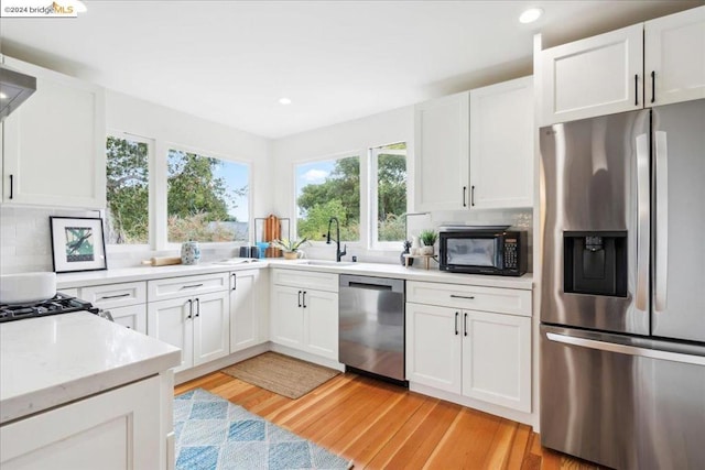 kitchen with sink, stainless steel appliances, tasteful backsplash, white cabinets, and light wood-type flooring