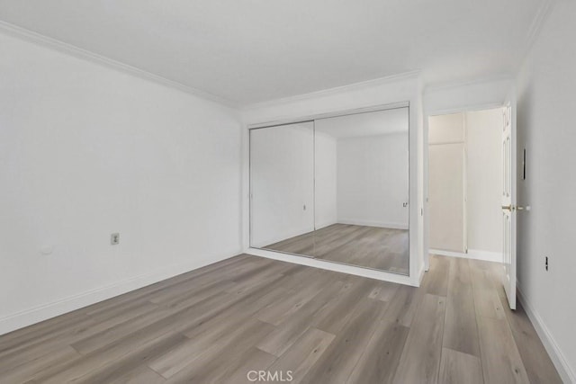 unfurnished bedroom with light wood-type flooring, a closet, and crown molding