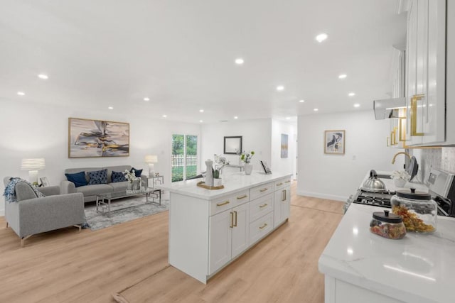 kitchen with ventilation hood, white cabinets, a kitchen island, light hardwood / wood-style flooring, and light stone counters