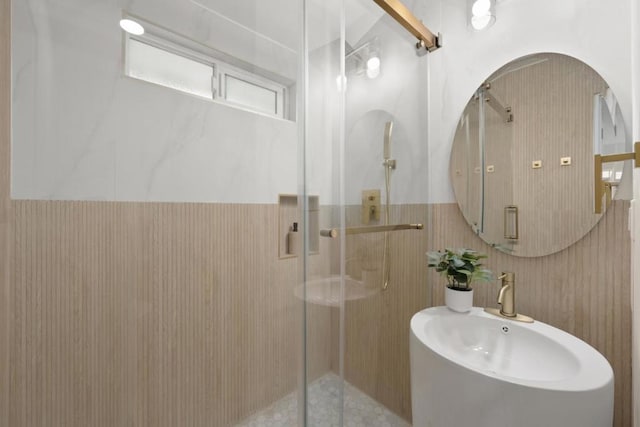 bathroom featuring a shower with shower door, tile walls, and sink