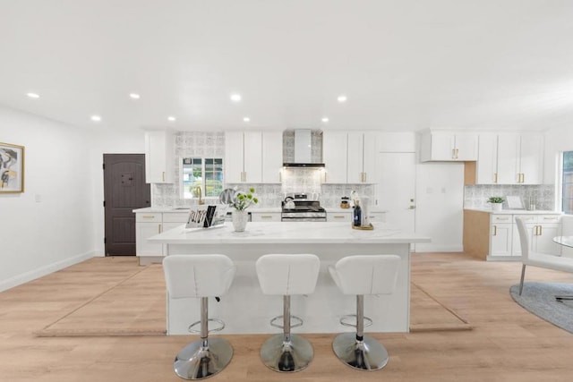 kitchen featuring stainless steel range oven, a kitchen island, a kitchen bar, white cabinetry, and wall chimney range hood