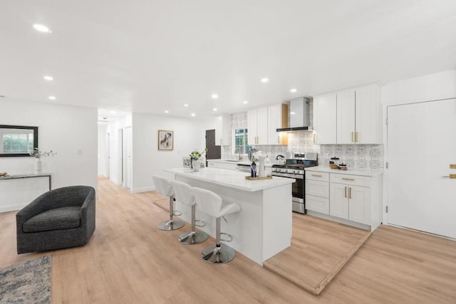 kitchen featuring white cabinetry, stainless steel range, wall chimney range hood, and an island with sink