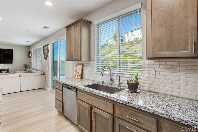 kitchen with light hardwood / wood-style floors, tasteful backsplash, stainless steel dishwasher, light stone counters, and sink