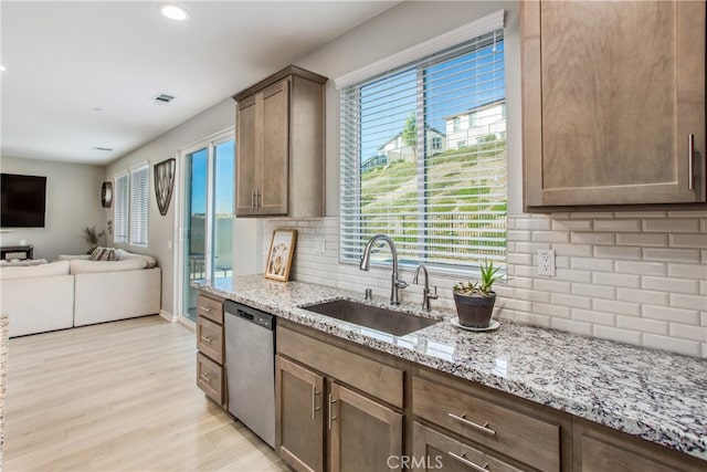 kitchen featuring stainless steel dishwasher, open floor plan, a sink, and a healthy amount of sunlight