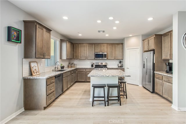 kitchen featuring light stone countertops, appliances with stainless steel finishes, a center island, a kitchen bar, and sink