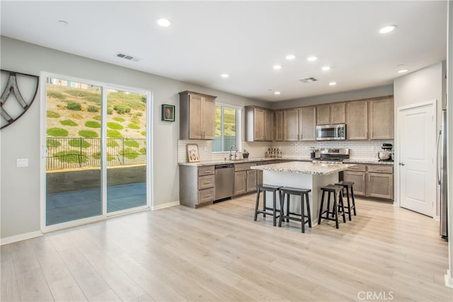 kitchen with stainless steel appliances, light wood-type flooring, light stone countertops, a kitchen island, and a breakfast bar