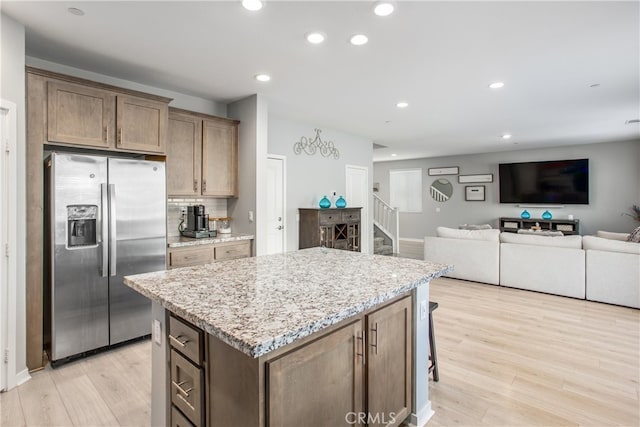 kitchen with light hardwood / wood-style flooring, stainless steel fridge, light stone counters, and a center island