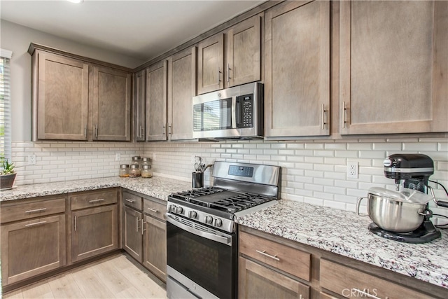 kitchen featuring light stone counters, backsplash, appliances with stainless steel finishes, and light wood-type flooring