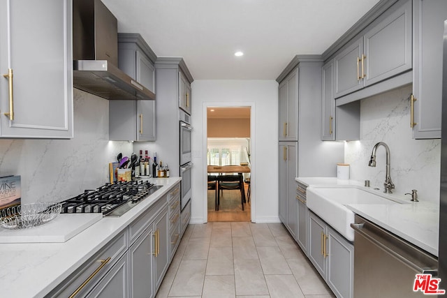 kitchen with backsplash, light stone counters, wall chimney exhaust hood, stainless steel appliances, and sink