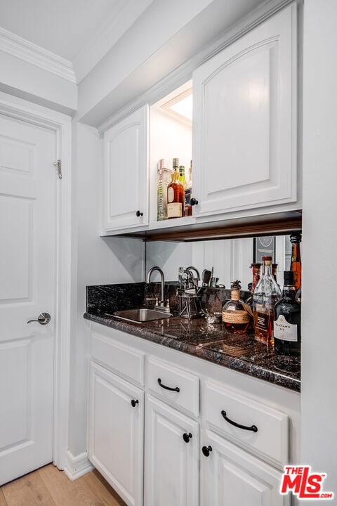 bar with white cabinetry, sink, dark stone countertops, crown molding, and light wood-type flooring