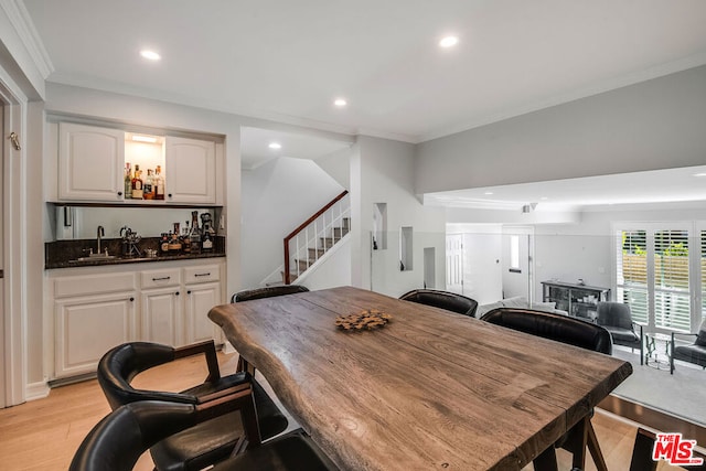 dining room with light hardwood / wood-style floors, crown molding, and indoor wet bar