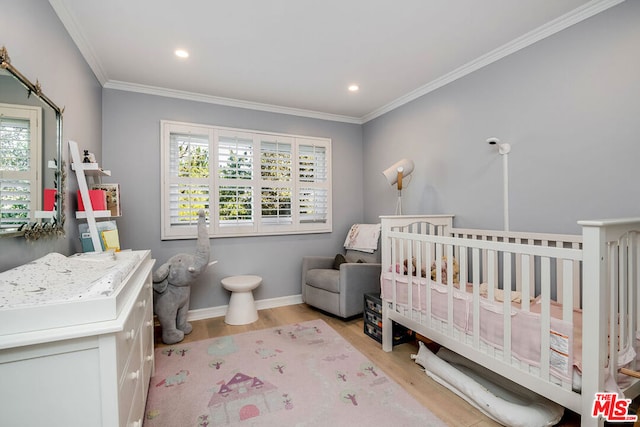 bedroom featuring multiple windows, light hardwood / wood-style floors, a nursery area, and ornamental molding