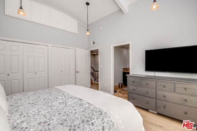 bedroom featuring two closets, beam ceiling, high vaulted ceiling, and light hardwood / wood-style flooring